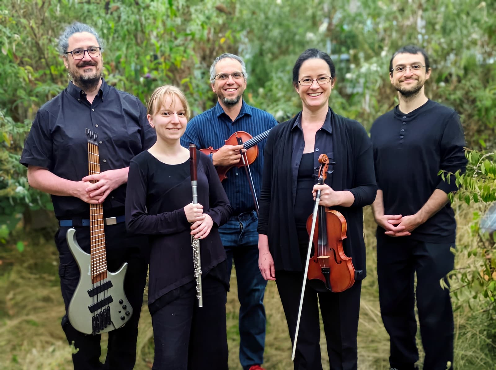 The five members of Pleasantly Frantic standing in a garden with a bass, a flute, and two fiddles